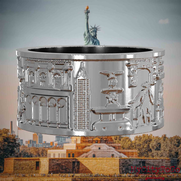 Silberner Ring mit Reliefs bekannter Sehenswürdigkeiten der Stadt New York. Den Hintergrund bildet eine Ansicht der Stadt New York.