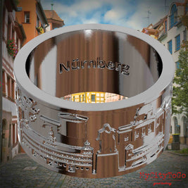 Versilberter Ring mit Reliefs bekannter Sehenswürdigkeiten der Stadt Nuernberg und einer Gravur des Stadtnamens auf der Innenseite. Den Hintergrund bildet eine Ansicht der Stadt  Nuernberg.