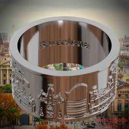 Versilberter Ring mit Reliefs bekannter Sehenswürdigkeiten der Stadt Barcelona und einer Gravur des Stadtnamens auf der Innenseite. Den Hintergrund bildet eine Ansicht der Stadt Barcelona.