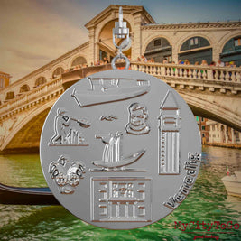 Halskette mit Drehwirbel und Rückseite eines silbernen Schmuckanhängers, auf dem Reliefs bekannter Sehenswürdigkeiten der Stadt Venedig abgebildet sind. Den Hintergrund bildet eine Ansicht der Stadt Venedig.
