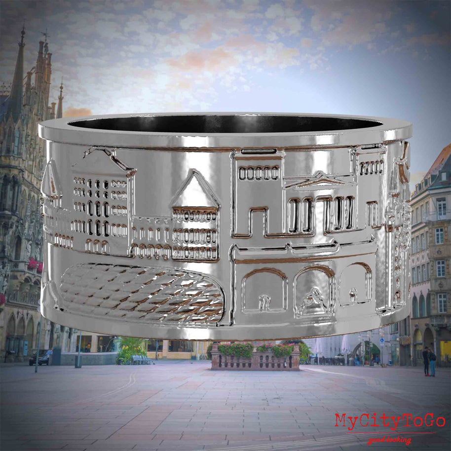Silberner Ring mit Reliefs bekannter Sehenswürdigkeiten der Stadt Muenchen. Den Hintergrund bildet eine Ansicht der Stadt Muenchen.