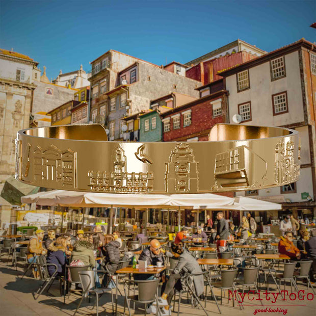 Vergoldeter Armreif mit Reliefs bekannter Sehenswürdigkeiten der Stadt Porto. Den Hintergrund bildet eine Ansicht der Stadt Porto.
