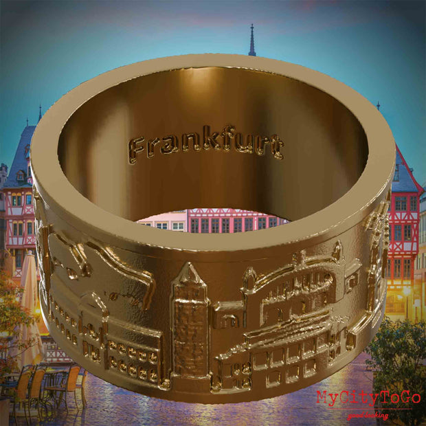 Vergoldeter Ring aus Edelstahl mit Reliefs bekannter Sehenswürdigkeiten der Stadt Frankfurt und einer Gravur des Stadtnamens auf der Innenseite. Den Hintergrund bildet eine Ansicht der Stadt Frankfurt.