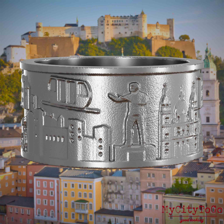 Ring aus Edelstahl mit Reliefs bekannter Sehenswürdigkeiten der Stadt Salzburg. Den Hintergrund bildet eine Ansicht der Stadt Salzburg.