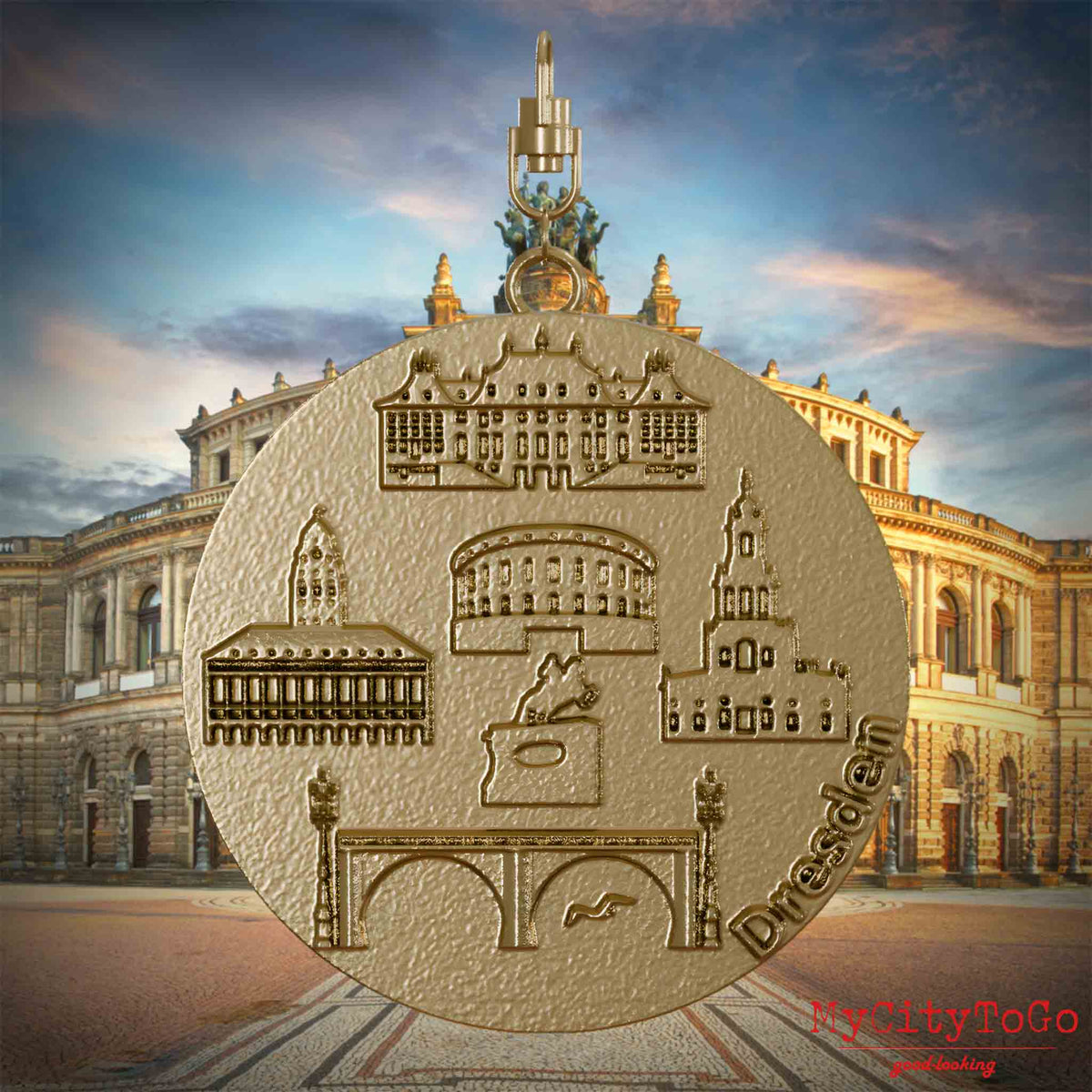 Halskette mit Drehwirbel und Vorderseite eines Schmuckanhängers aus vergoldetem Edelstahl, auf dem Reliefs bekannter Sehenswürdigkeiten der Stadt Dresden abgebildet sind. Den Hintergrund bildet eine Ansicht der Stadt Dresden.