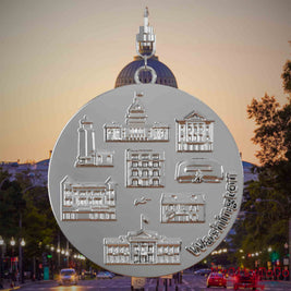 Halskette mit Drehwirbel und Rückseite eines silbernen Schmuckanhängers, auf dem Reliefs bekannter Sehenswürdigkeiten der Stadt Washington abgebildet sind. Den Hintergrund bildet eine Ansicht der Stadt Washington.
