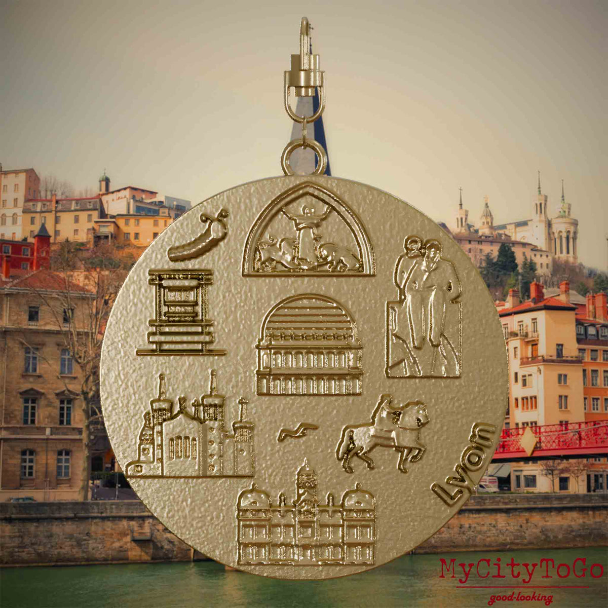 Halskette mit Drehwirbel und Rückseite eines Schmuckanhängers aus vergoldetem Edelstahl, auf dem Reliefs bekannter Sehenswürdigkeiten der Stadt Lyon abgebildet sind. Den Hintergrund bildet eine Ansicht der Stadt Lyon.
