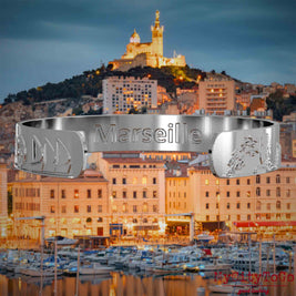 Innenseite eines silbernen Armreifs mit Reliefs bekannter Sehenswürdigkeiten der Stadt Marseille und einer Gravur des Stadtnamens. Den Hintergrund bildet eine Ansicht der Stadt Marseille.