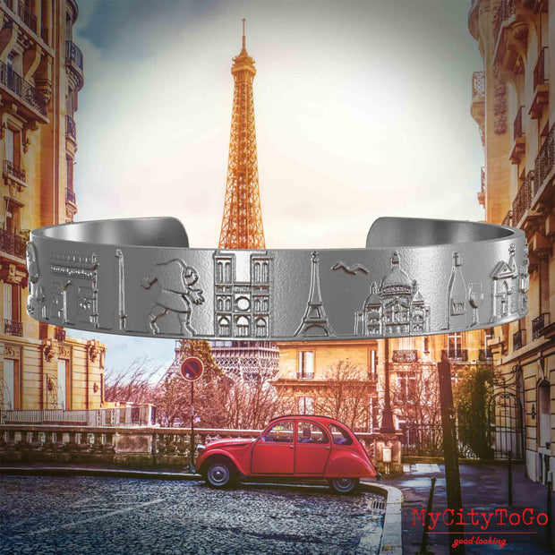 Armreif aus Edelstahl mit Reliefs bekannter Sehenswürdigkeiten der Stadt Paris. Den Hintergrund bildet eine Ansicht der Stadt Paris.