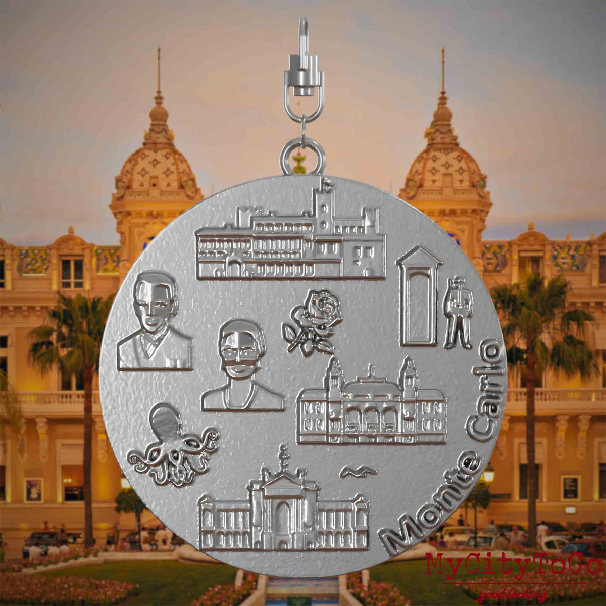 Halskette mit Drehwirbel und Rückseite eines Schmuckanhängers aus Edelstahl, auf dem Reliefs bekannter Sehenswürdigkeiten der Stadt Monte Carlo abgebildet sind. Den Hintergrund bildet eine Ansicht der Stadt Monte Carlo .
