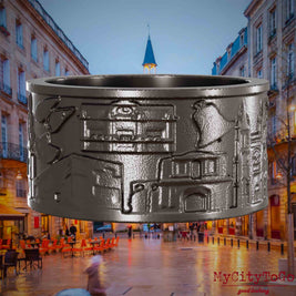 Ring aus Titan mit Reliefs bekannter Sehenswürdigkeiten der Stadt Bordeaux. Den Hintergrund bildet eine Ansicht der Stadt Bordeaux.