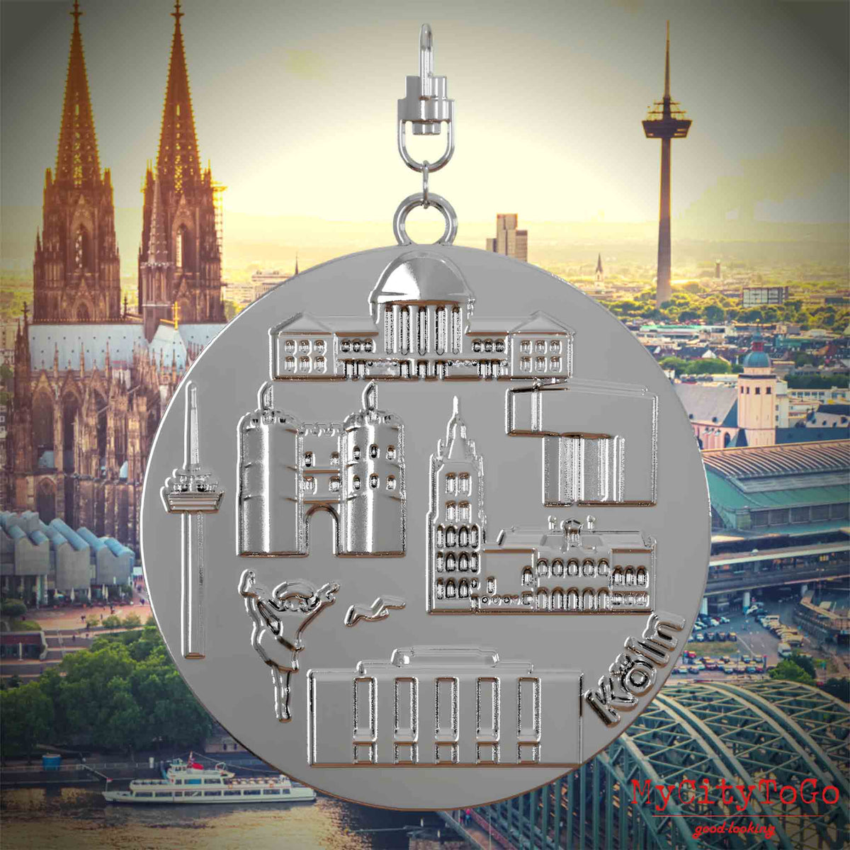 Halskette mit Drehwirbel und Rückseite eines silbernen Schmuckanhängers, auf dem Reliefs bekannter Sehenswürdigkeiten der Stadt Koeln abgebildet sind. Den Hintergrund bildet eine Ansicht der Stadt Koeln.