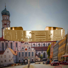 Vergoldeter Armreif mit Reliefs bekannter Sehenswürdigkeiten der Stadt Augsburg. Den Hintergrund bildet eine Ansicht der Stadt Augsburg.
