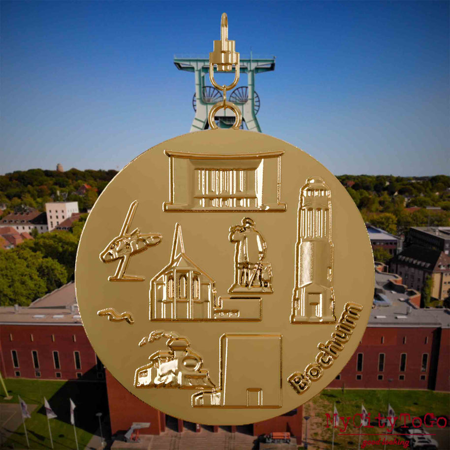 Halskette mit Drehwirbel und Rückseite eines vergoldeten Schmuckanhängers, auf dem Reliefs bekannter Sehenswürdigkeiten der Stadt Bochum abgebildet sind. Den Hintergrund bildet eine Ansicht der Stadt Bochum .
