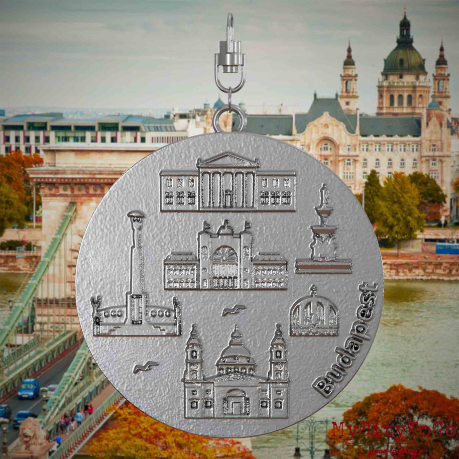 Halskette mit Drehwirbel und Rückseite eines Schmuckanhängers aus Edelstahl, auf dem Reliefs bekannter Sehenswürdigkeiten der Stadt Budapest abgebildet sind. Den Hintergrund bildet eine Ansicht der Stadt Budapest.
