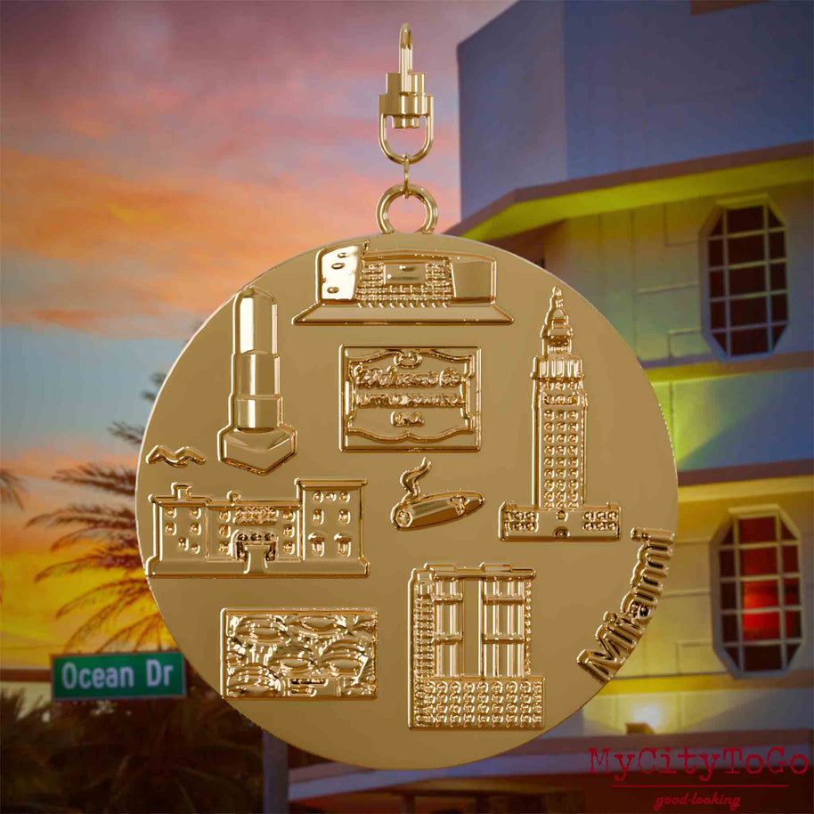 Halskette mit Drehwirbel und Vorderseite eines vergoldeten Schmuckanhängers, auf dem Reliefs bekannter Sehenswürdigkeiten der Stadt Miami abgebildet sind. Den Hintergrund bildet eine Ansicht der Stadt Miami.
