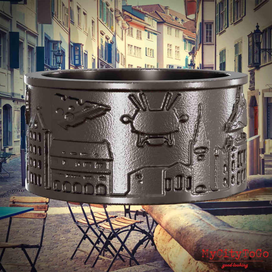 Ring aus Titan mit Reliefs bekannter Sehenswürdigkeiten der Stadt Zuerich. Den Hintergrund bildet eine Ansicht der Stadt Zuerich.