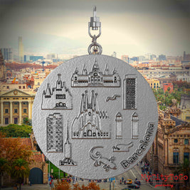 Halskette mit Drehwirbel und Rückseite eines Schmuckanhängers aus Edelstahl, auf dem Reliefs bekannter Sehenswürdigkeiten der Stadt Barcelona abgebildet sind. Den Hintergrund bildet eine Ansicht der Stadt Barcelona.
