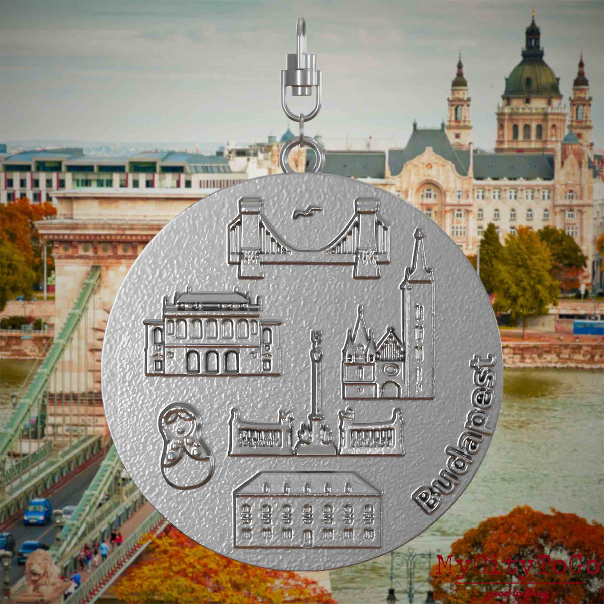 Halskette mit Drehwirbel und Vorderseite eines Schmuckanhängers aus Edelstahl, auf dem Reliefs bekannter Sehenswürdigkeiten der Stadt Budapest abgebildet sind. Den Hintergrund bildet eine Ansicht der Stadt Budapest.
