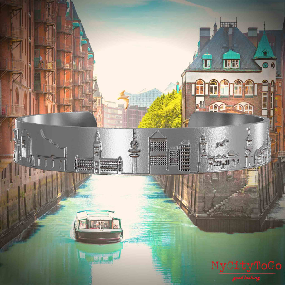 Stainless steel bangle with reliefs of well-known landmarks in the city of Hamburg. The background features a view of the city of Hamburg.