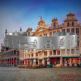 Armreif aus Edelstahl mit Reliefs bekannter Sehenswürdigkeiten der Stadt Brüssel. Den Hintergrund bildet eine Ansicht der Stadt Bruessel.