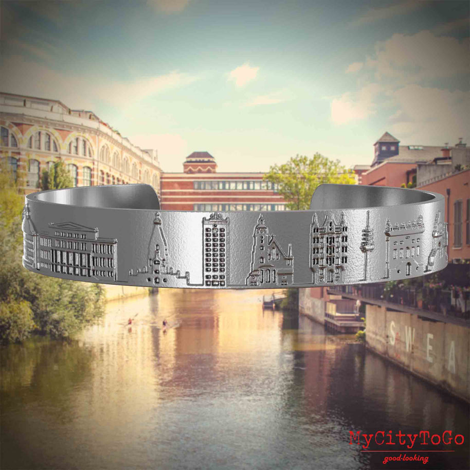 Armreif aus Edelstahl mit Reliefs bekannter Sehenswürdigkeiten der Stad Leipzig. Den Hintergrund bildet eine Ansicht der Stadt Leipzig.