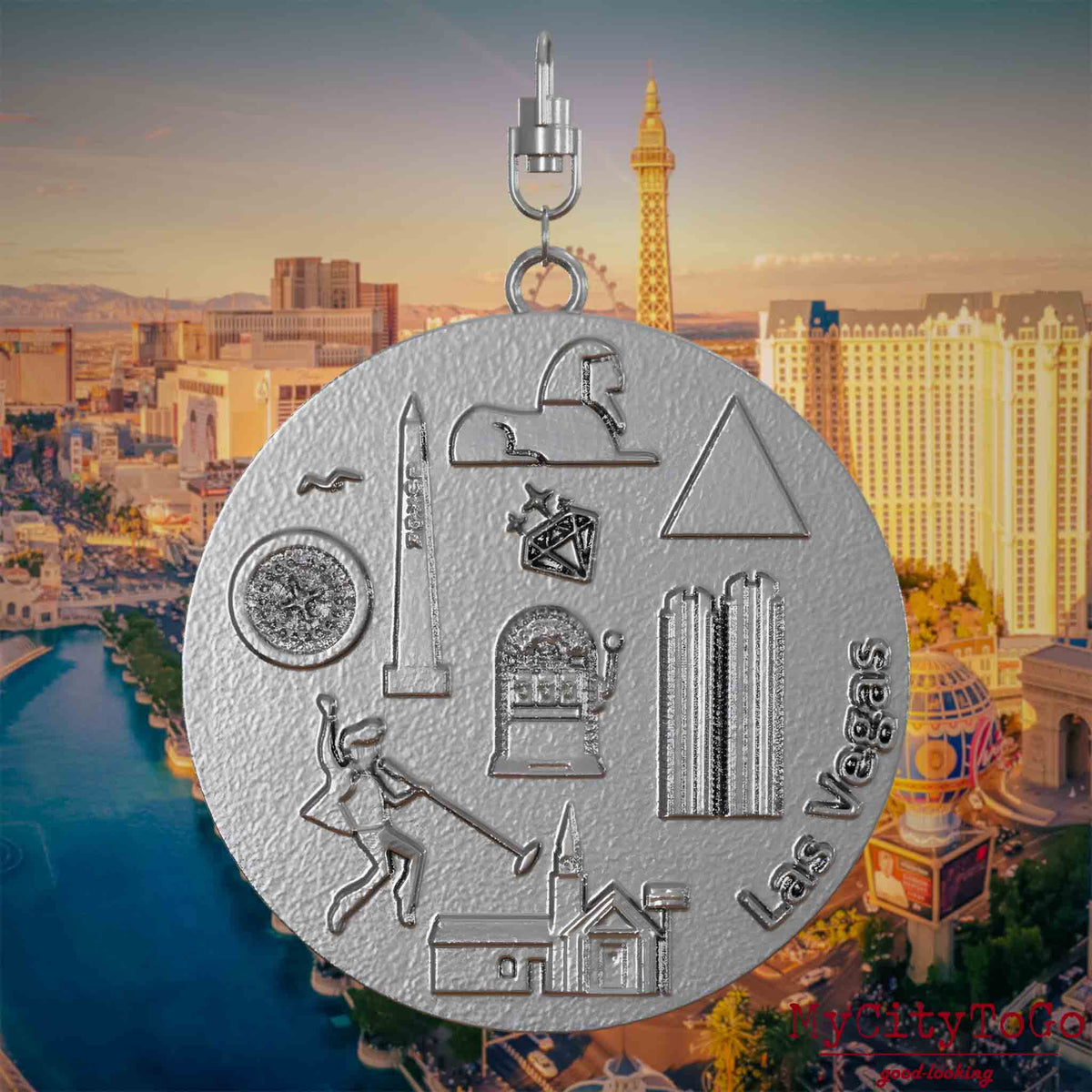 Necklace with swivel clasp and front of a stainless steel jewelry pendant featuring reliefs of famous Las Vegas landmarks. The background shows a view of the city of Las Vegas.