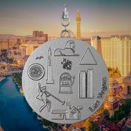 Necklace with swivel clasp and front of a stainless steel jewelry pendant featuring reliefs of famous Las Vegas landmarks. The background shows a view of the city of Las Vegas.