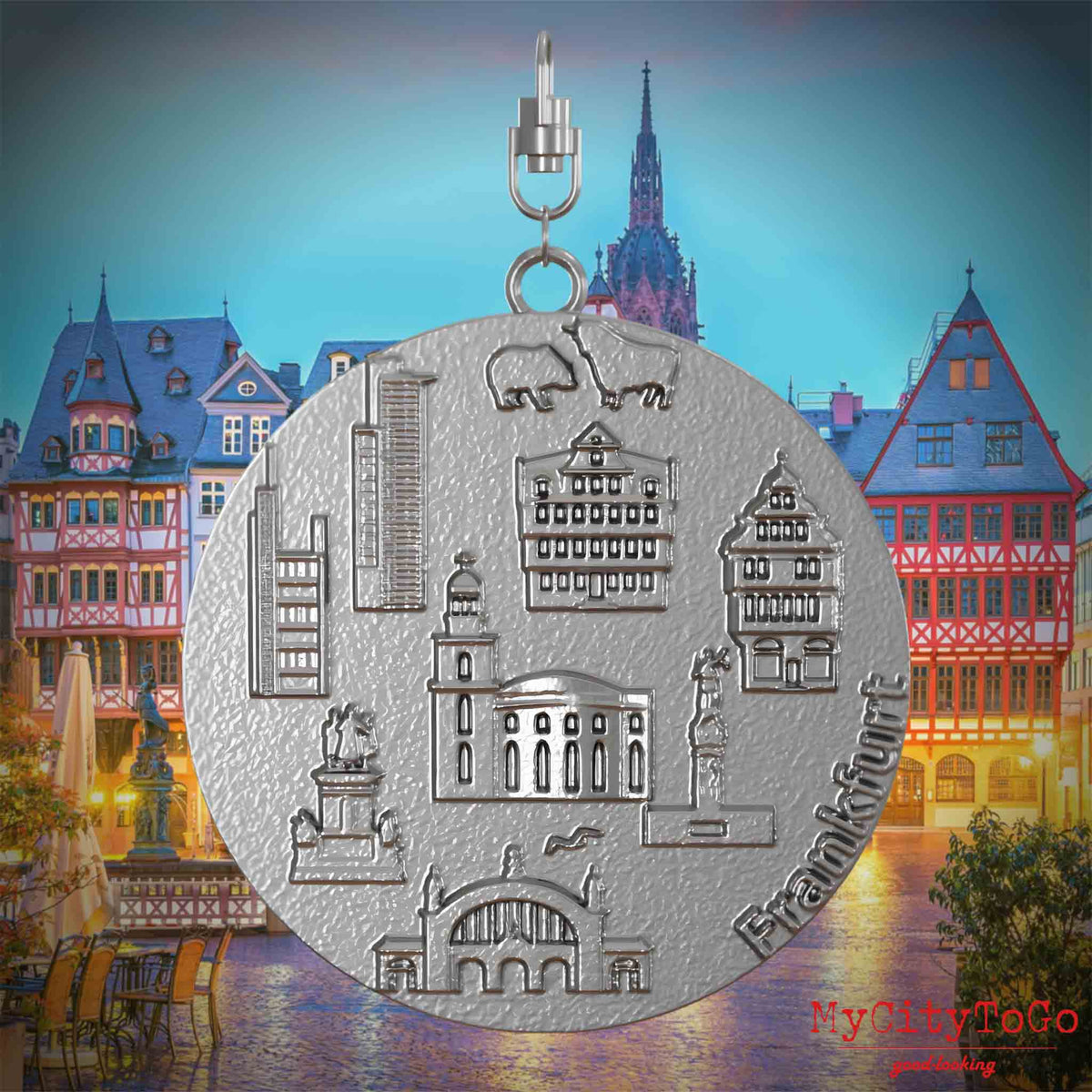 Halskette mit Drehwirbel und Vorderseite eines Schmuckanhängers aus Edelstahl, auf dem Reliefs bekannter Sehenswürdigkeiten der Stadt Frankfurt abgebildet sind. Den Hintergrund bildet eine Ansicht der Stadt Frankfurt.
