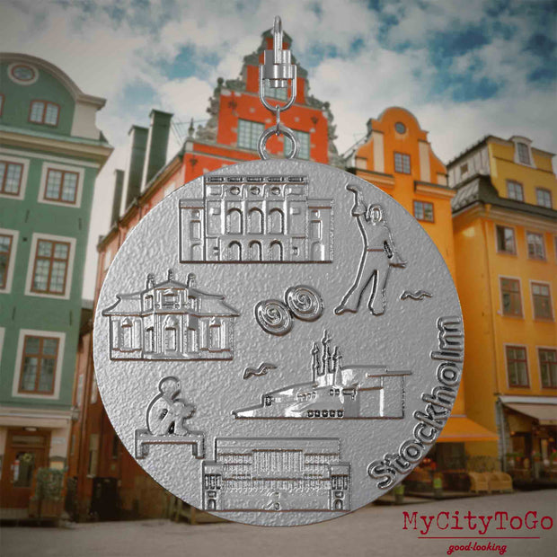 Halskette mit Drehwirbel und Vorderseite eines Schmuckanhängers aus Edelstahl, auf dem Reliefs bekannter Sehenswürdigkeiten der Stadt Stockholm abgebildet sind. Den Hintergrund bildet eine Ansicht der Stadt Stockholm.
