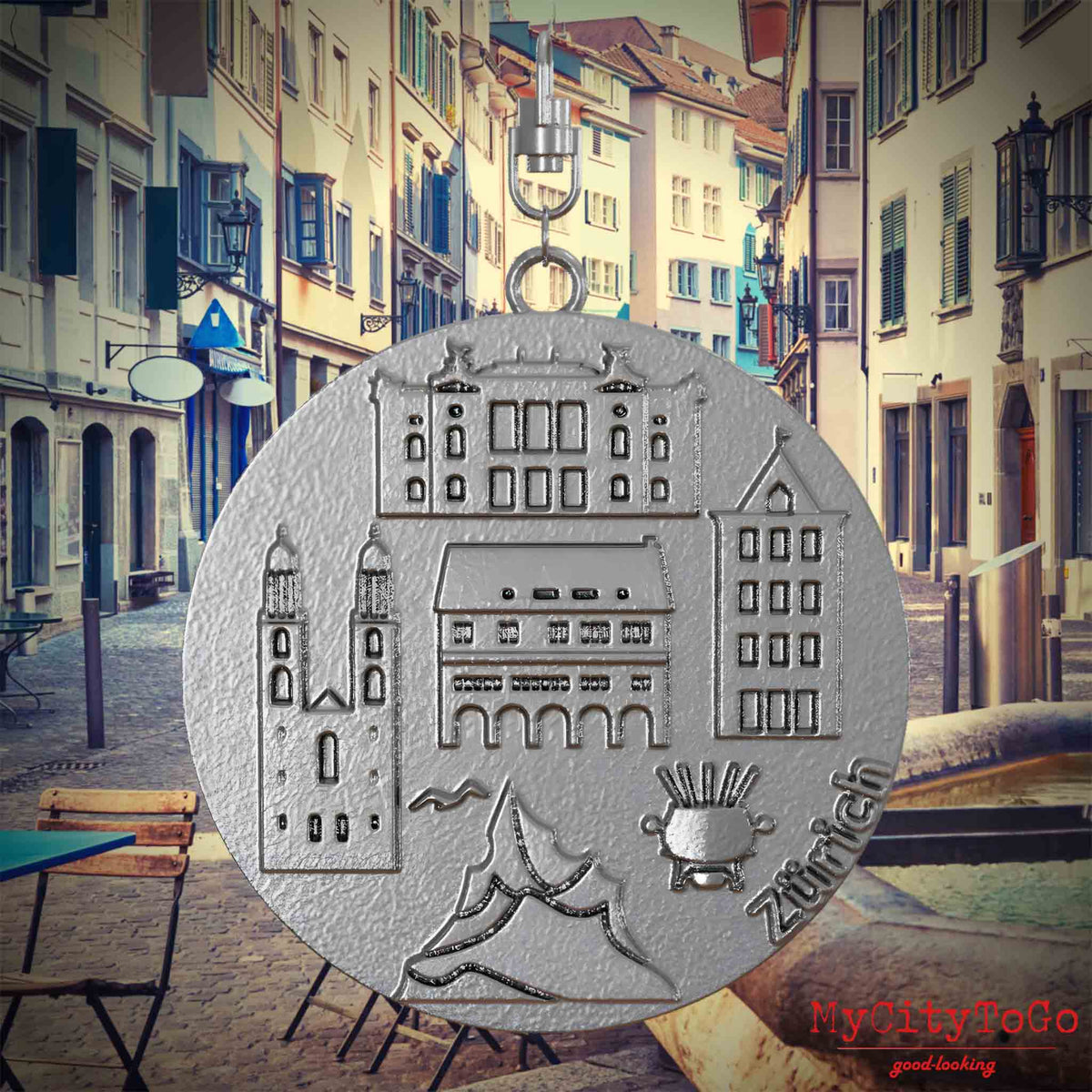 Halskette mit Drehwirbel und Vorderseite eines Schmuckanhängers aus Edelstahl, auf dem Reliefs bekannter Sehenswürdigkeiten der Stadt Zuerich abgebildet sind. Den Hintergrund bildet eine Ansicht der Stadt Zuerich.
