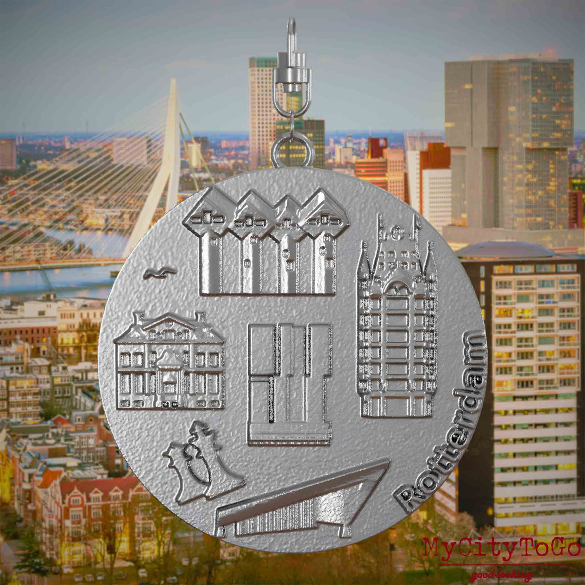 Halskette mit Drehwirbel und Vorderseite eines Schmuckanhängers aus Edelstahl, auf dem Reliefs bekannter Sehenswürdigkeiten der Stadt Rotterdam abgebildet sind. Den Hintergrund bildet eine Ansicht der Stadt Rotterdam.

