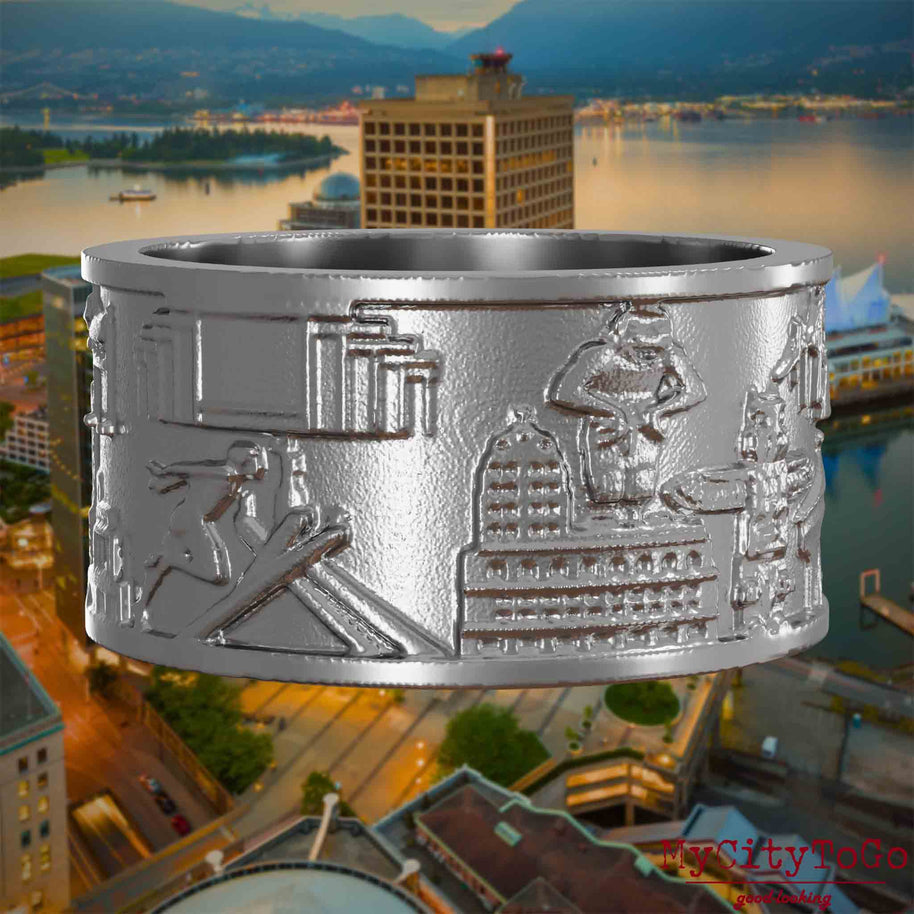 Ring aus Edelstahl mit Reliefs bekannter Sehenswürdigkeiten der Stadt Vancouver. Den Hintergrund bildet eine Ansicht der Stadt Vancouver.