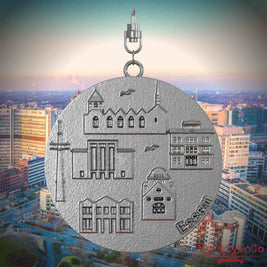 Halskette mit Drehwirbel und Vorderseite eines Schmuckanhängers aus Edelstahl, auf dem Reliefs bekannter Sehenswürdigkeiten der Stadt Essen abgebildet sind. Den Hintergrund bildet eine Ansicht der Stadt Essen.