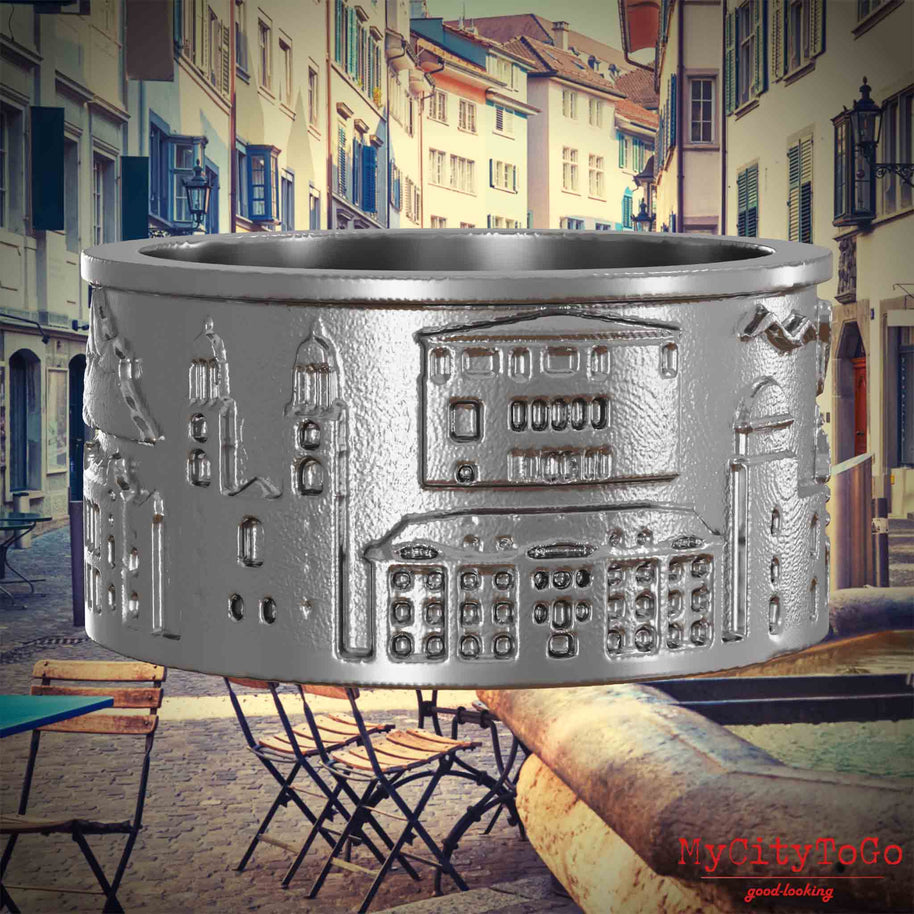 Ring aus Edelstahl mit Reliefs bekannter Sehenswürdigkeiten der Stadt Zuerich. Den Hintergrund bildet eine Ansicht der Stadt Zuerich.