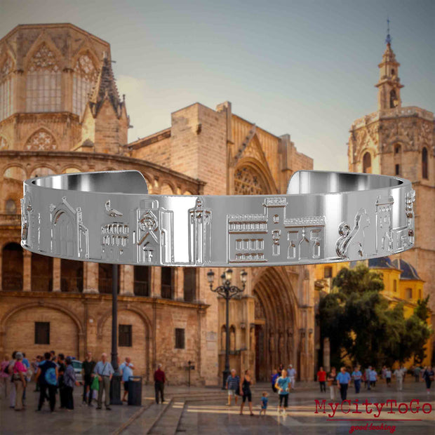 Versilberter Armreif mit Reliefs bekannter Sehenswürdigkeiten der Stadt Valencia. Den Hintergrund bildet eine Ansicht der Stadt Valencia.