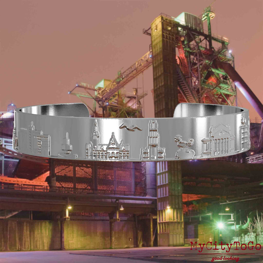 Silver-plated Bangle with reliefs of well-known landmarks of the city of Duisburg. The background features a view of the city of Duisburg.