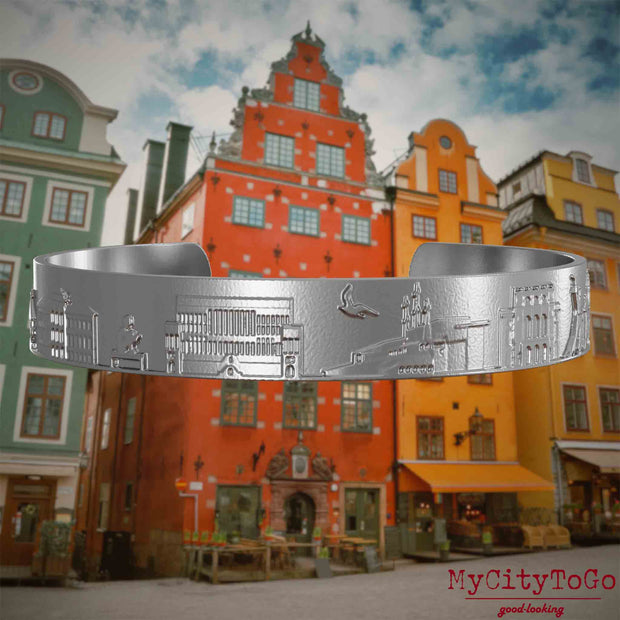Armreif aus Edelstahl mit Reliefs bekannter Sehenswürdigkeiten der Stadt Stockholm. Den Hintergrund bildet eine Ansicht der Stadt Stockholm.