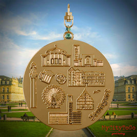 Halskette mit Drehwirbel und Rückseite eines vergoldeten Schmuckanhängers, auf dem Reliefs bekannter Sehenswürdigkeiten der Stadt Stuttgart abgebildet sind. Den Hintergrund bildet eine Ansicht der Stadt Stuttgart.
