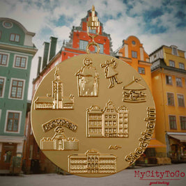 Halskette mit Drehwirbel und Rückseite eines vergoldeten Schmuckanhängers, auf dem Reliefs bekannter Sehenswürdigkeiten der Stadt Stockholm abgebildet sind. Den Hintergrund bildet eine Ansicht der Stadt Stockholm.
