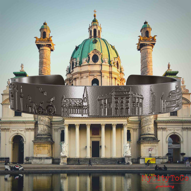 Armreif aus Titan mit Reliefs bekannter Sehenswürdigkeiten der Stadt Wien. Den Hintergrund bildet eine Ansicht der Stadt Wien.