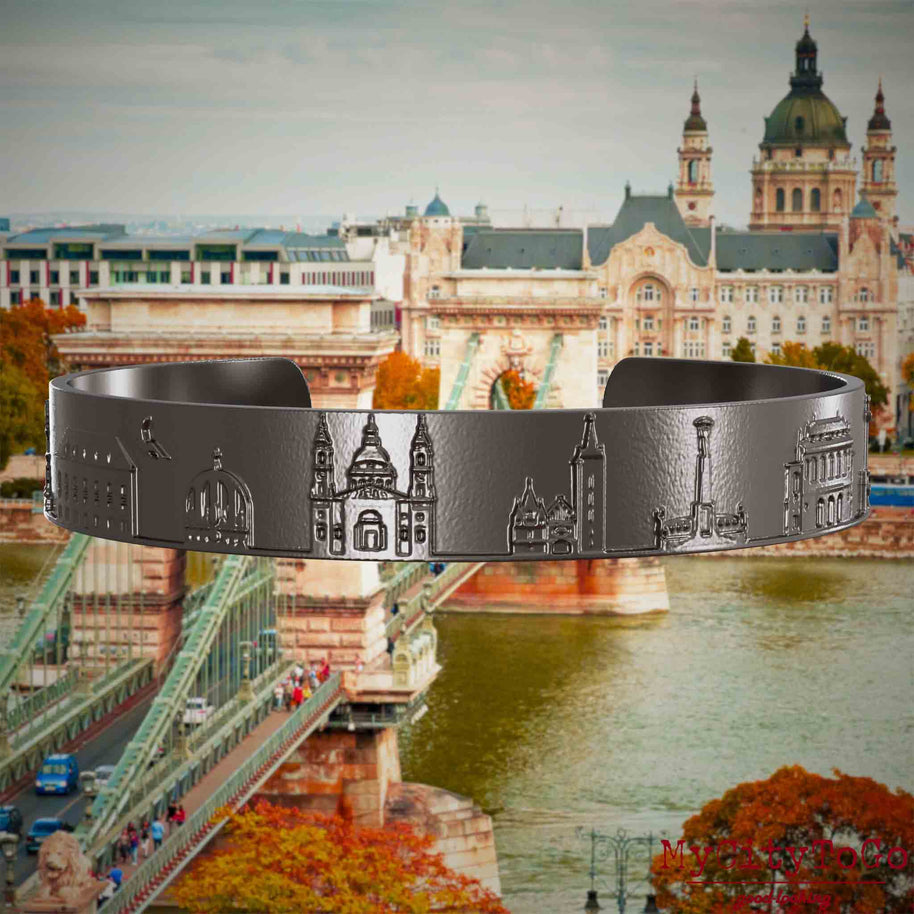 Armreif aus Titan mit Reliefs bekannter Sehenswürdigkeiten der Stadt Budapest. Den Hintergrund bildet eine Ansicht der Stadt Budapest.