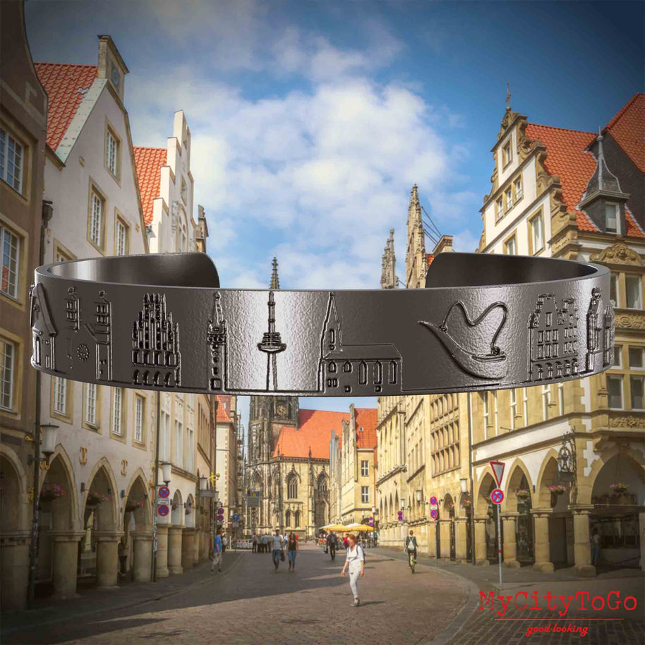 Armreif aus Titan mit Reliefs bekannter Sehenswürdigkeiten der Stadt Muenster. Den Hintergrund bildet eine Ansicht der Stadt Muenster.