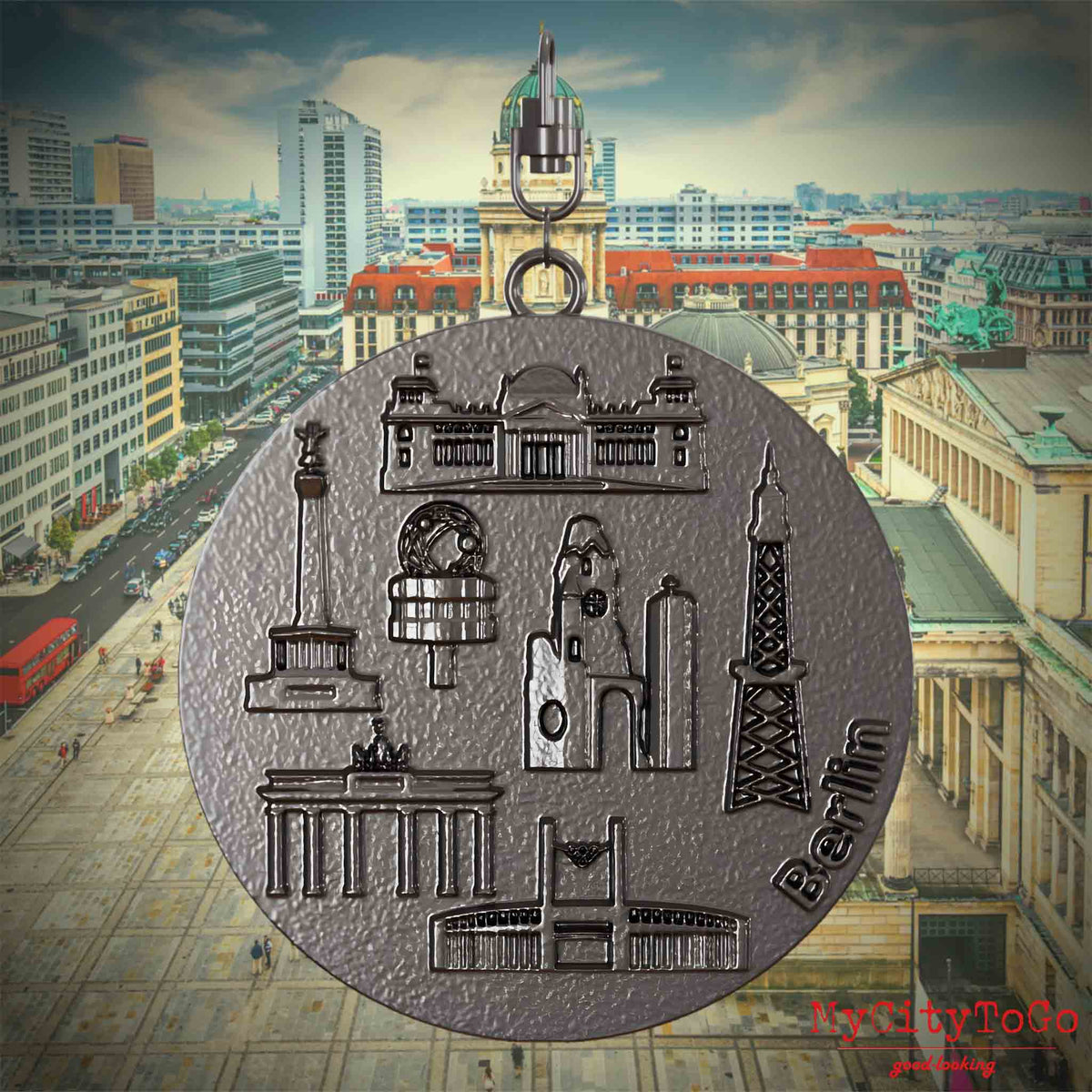 Halskette mit Drehwirbel und Rückseite eines Schmuckanhängers aus Titan, auf dem Reliefs bekannter Sehenswürdigkeiten der Stadt Berlin abgebildet sind. Den Hintergrund bildet eine Ansicht der Stadt Berlin.
