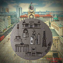Halskette mit Drehwirbel und Rückseite eines Schmuckanhängers aus Titan, auf dem Reliefs bekannter Sehenswürdigkeiten der Stadt Berlin abgebildet sind. Den Hintergrund bildet eine Ansicht der Stadt Berlin.