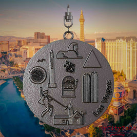 Necklace with swivel and front of a titanium jewelry pendant featuring reliefs of well-known Las Vegas landmarks. The background shows a view of the city of Las Vegas.