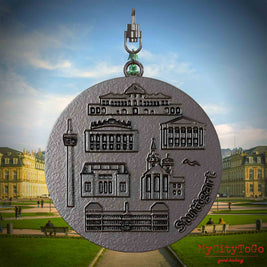 Halskette mit Drehwirbel und Vorderseite eines Schmuckanhängers aus Titan, auf dem Reliefs bekannter Sehenswürdigkeiten der Stadt Stuttgart abgebildet sind. Den Hintergrund bildet eine Ansicht der Stadt Stuttgart.
