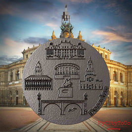 Halskette mit Drehwirbel und Vorderseite eines Schmuckanhängers aus Titan, auf dem Reliefs bekannter Sehenswürdigkeiten der Stadt Dresden abgebildet sind. Den Hintergrund bildet eine Ansicht der Stadt Dresden.