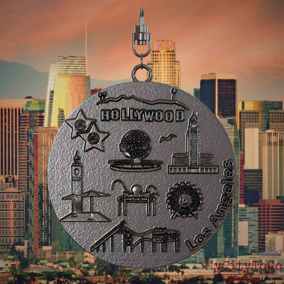 Halskette mit Drehwirbel und Vorderseite eines Schmuckanhängers aus Titan, auf dem Reliefs bekannter Sehenswürdigkeiten der Stadt Los Angeles abgebildet sind. Den Hintergrund bildet eine Ansicht der Stadt Los Angeles.
