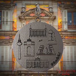 Halskette mit Drehwirbel und Vorderseite eines Schmuckanhängers aus Titan, auf dem Reliefs bekannter Sehenswürdigkeiten der Stadt Madrid abgebildet sind. Den Hintergrund bildet eine Ansicht der Stadt Madrid.
